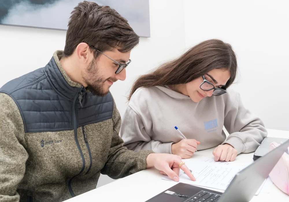 A Smart Space tutor sitting beside a high school student, pointing at her work on the desk while she writes